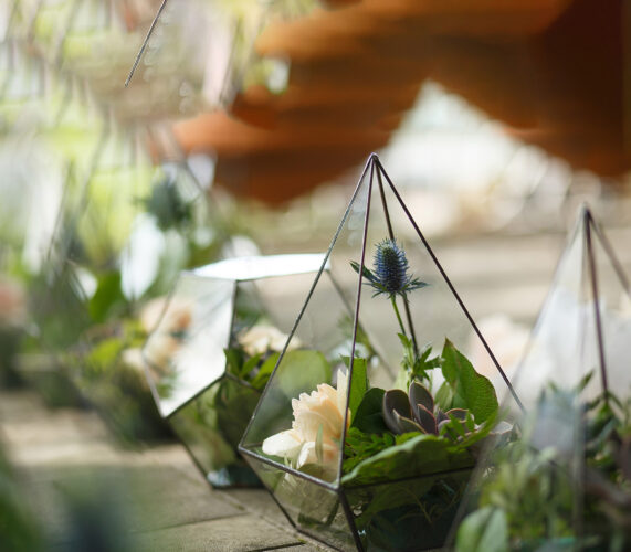 female florist puts fresh succulent and rose flowers in glass florarium. Event fresh flowers decoration. Florist workflow. Wedding banquet design